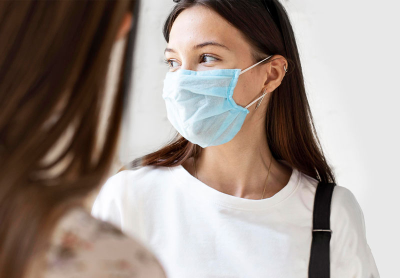 female student wearing a white top and a blue face mask while speaking to another female