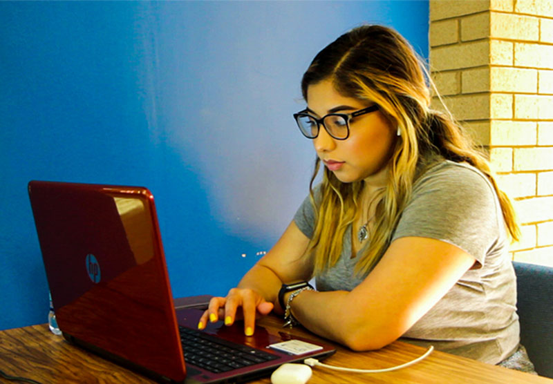 female student sitting at desk looking at a red laptop