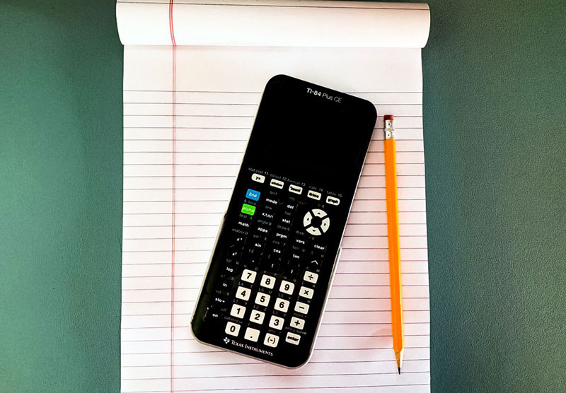 graphing calculator on desk with notebook and pencil