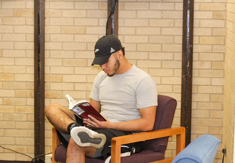 male student sitting at the library reading a book