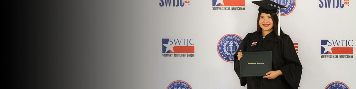 Student in graduation regalia posed in front of an SWTJC logo banner while holding their degree.