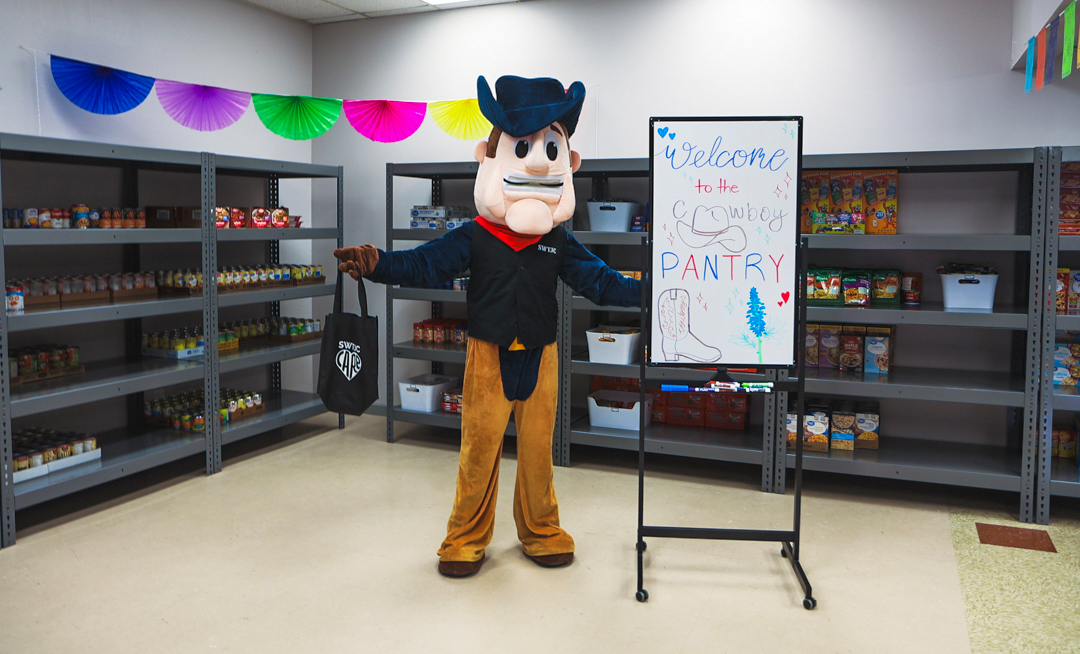 SWTJC Mascot Tex stands by a welcome sign at the Cowboy Food Pantry in Uvalde.